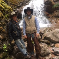 2 men standing with a waterfall behind them